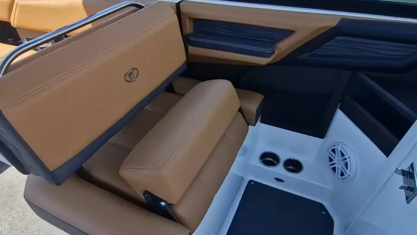 Interior of a boat showing plush brown seating, storage compartment, cup holders, and a speaker in a sleek design.